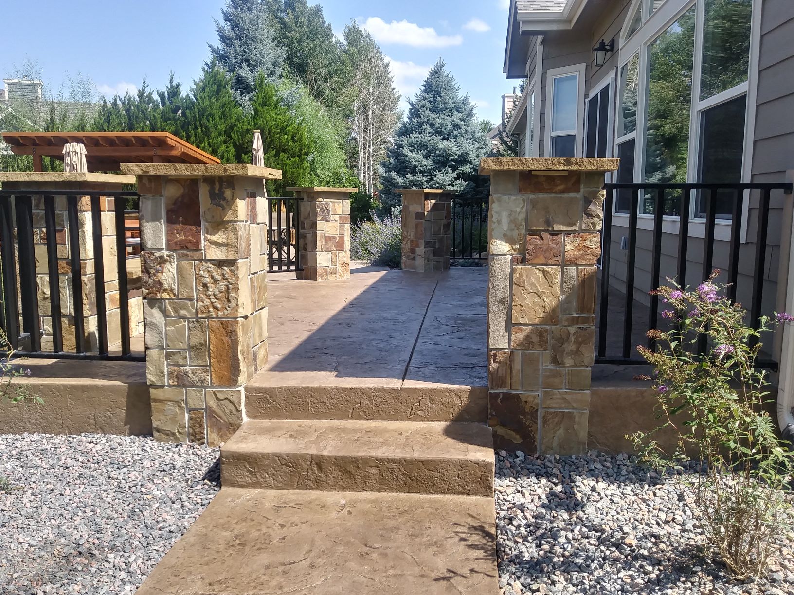 Printed concrete patio with stone pillars and concrete path surrounded by rocks.
