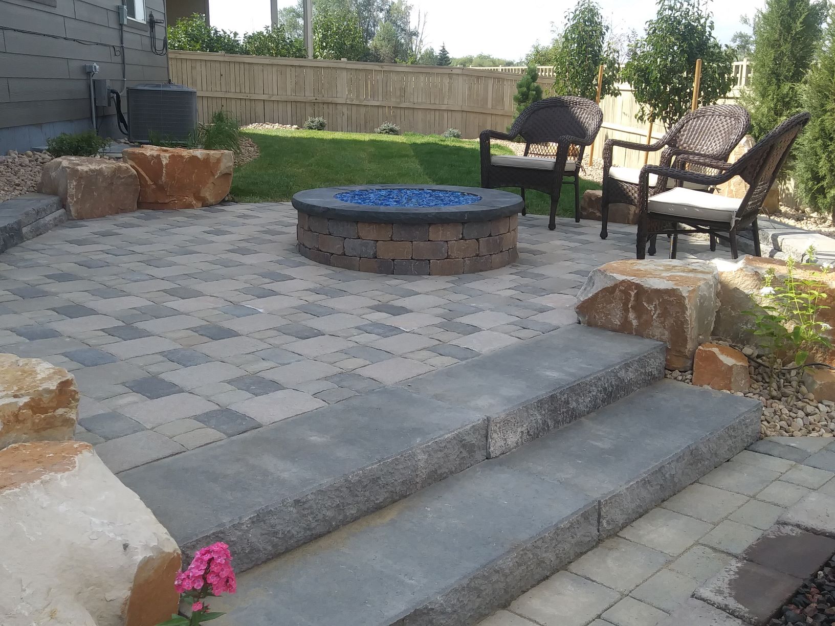 Brick laid patio with flat stone steps and bright blue rock pit in the center.