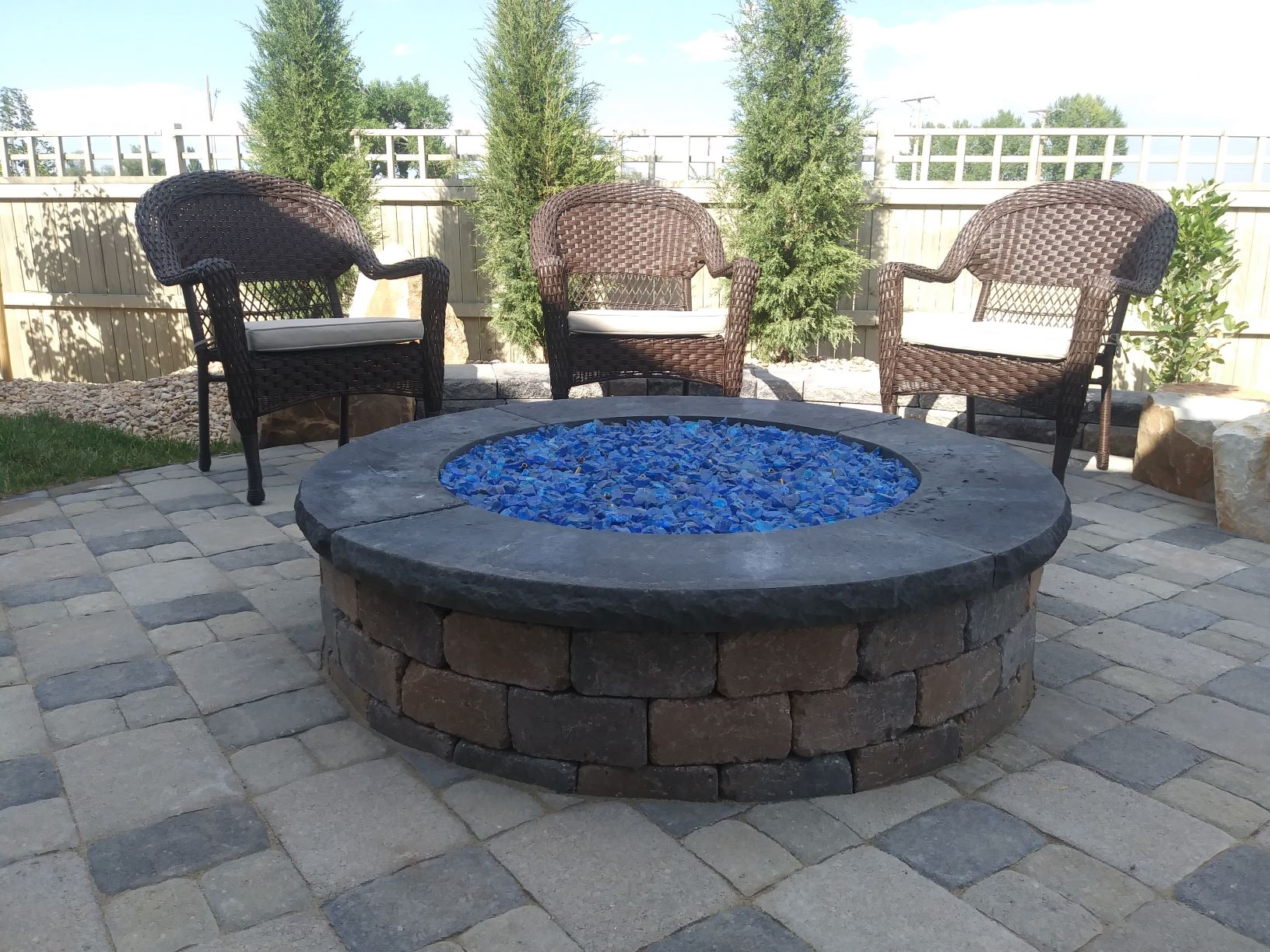Center Bright blue rock pit with brick laid patio and seating area.