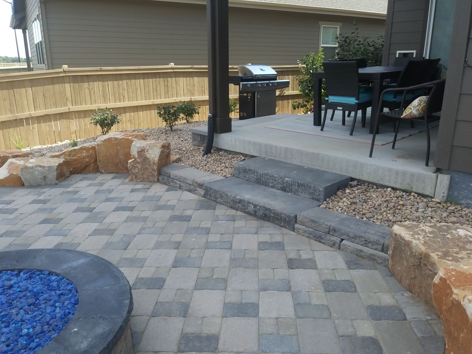 Brick laid patio with flat stone steps and rocks with boulders on the edge.