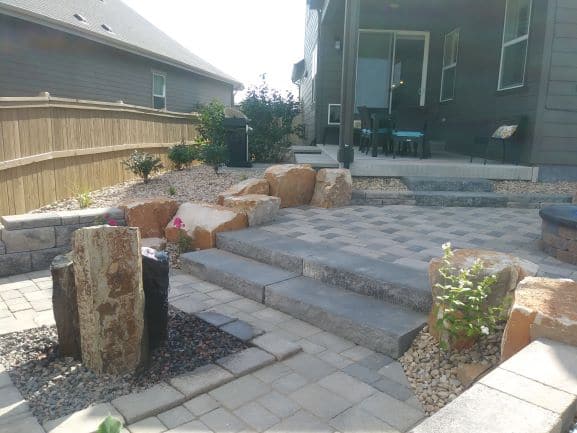 Brick laid patio with water feature and stone steps surrounded by boulders and rocks.