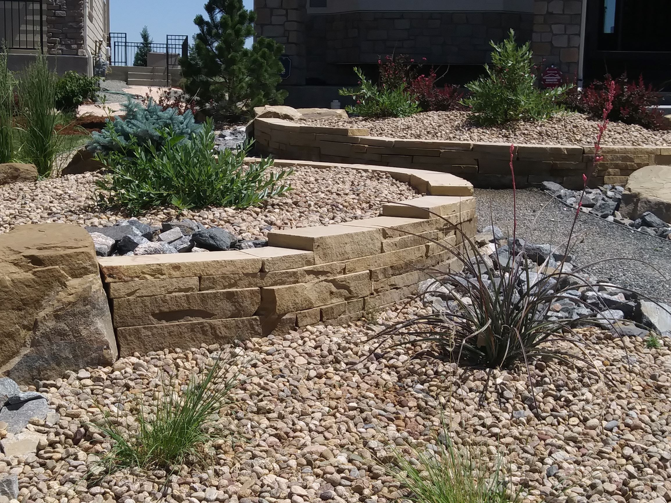 Large rocks and brick edged raised beds. Multiple bushes and plants through out.