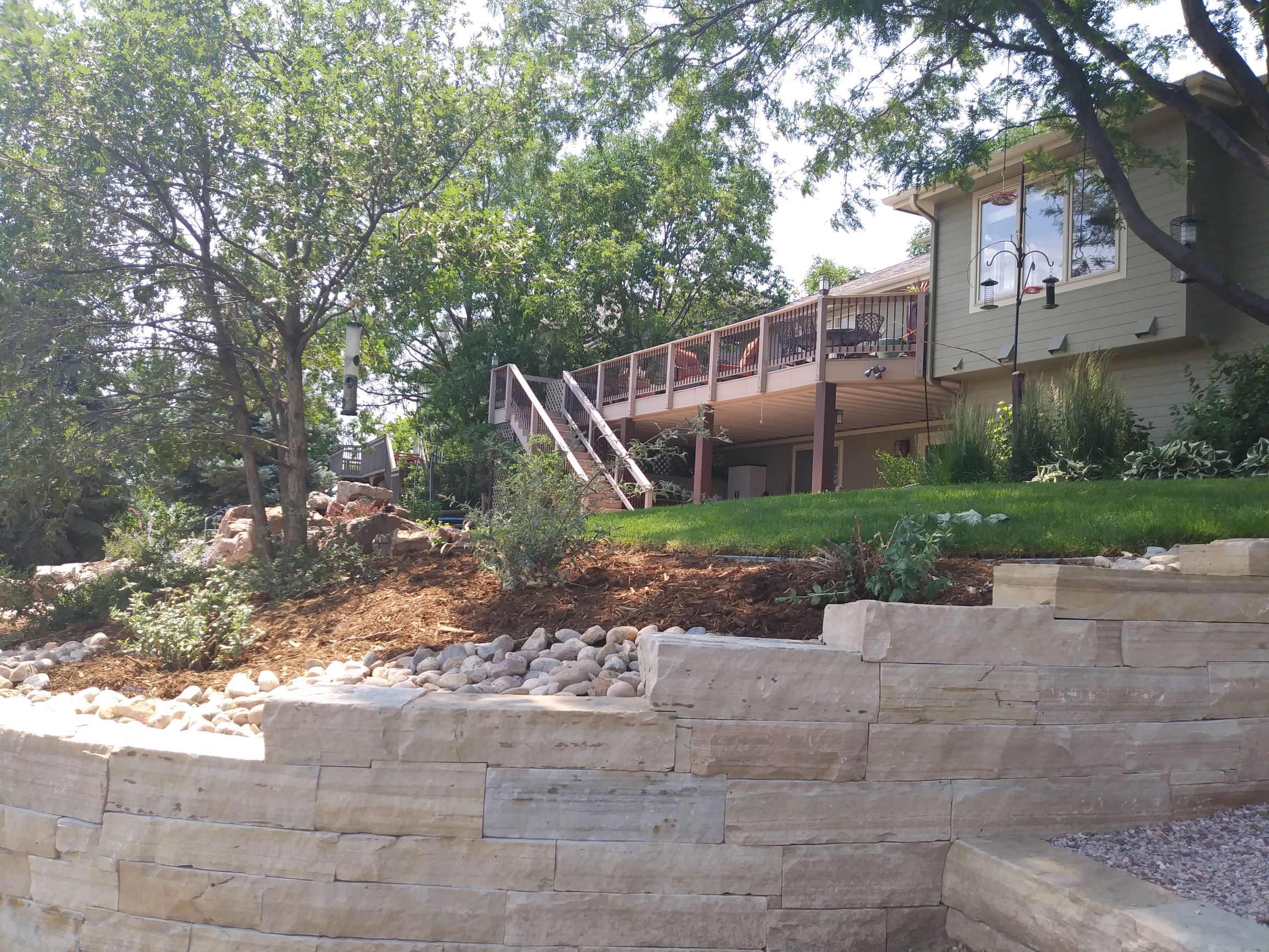 Flat stone retaining wall. large rocks and mulch with plants and bushes placed through out.