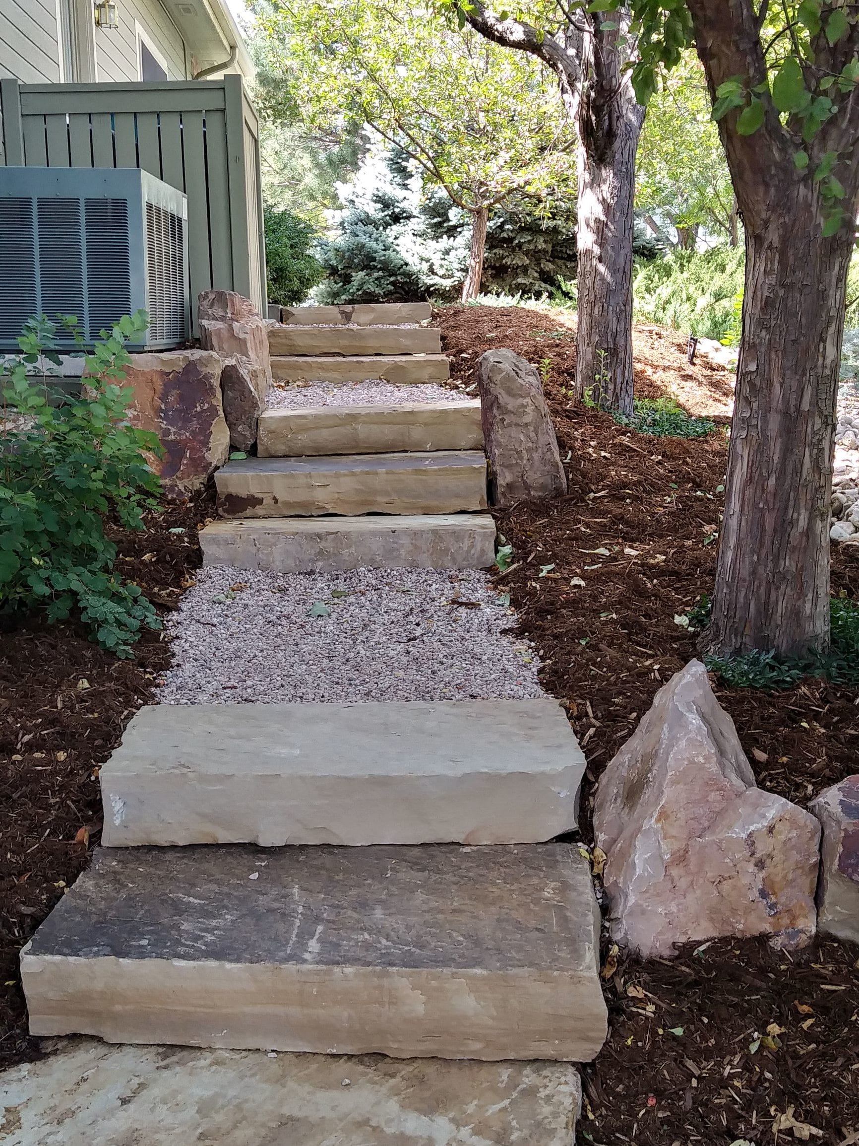 Gravel path with stone steps bordered with large decorative rock.