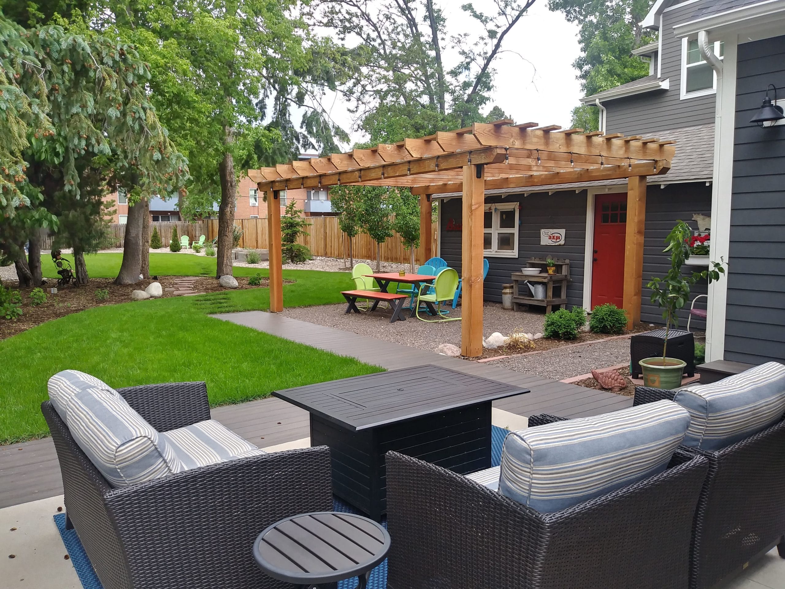 Small gravel patio with seating and pergola over head with grass and trees all around.