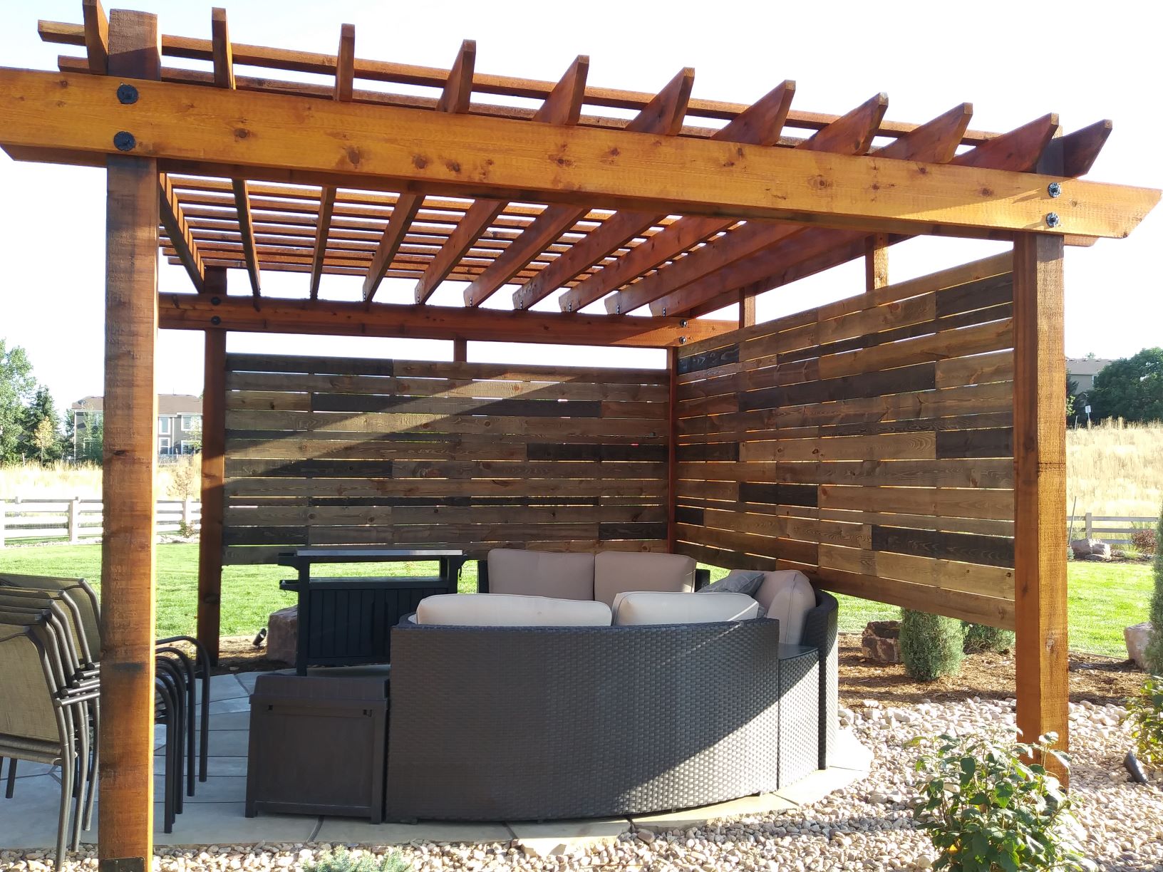 Pergola over flat stone patio with seating and a wind/privacy wall.