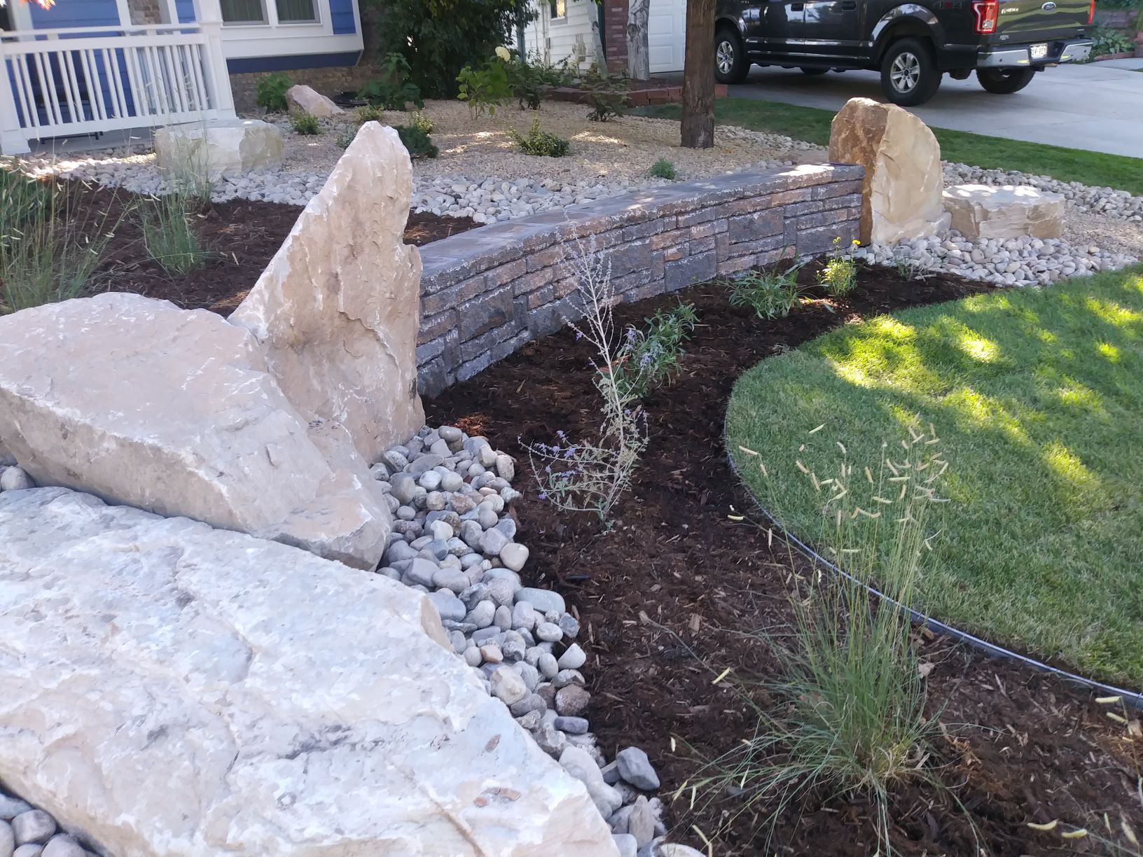 Boulders and large rocks with mulch, edging, and green grass with low maintenance plants and bushes.