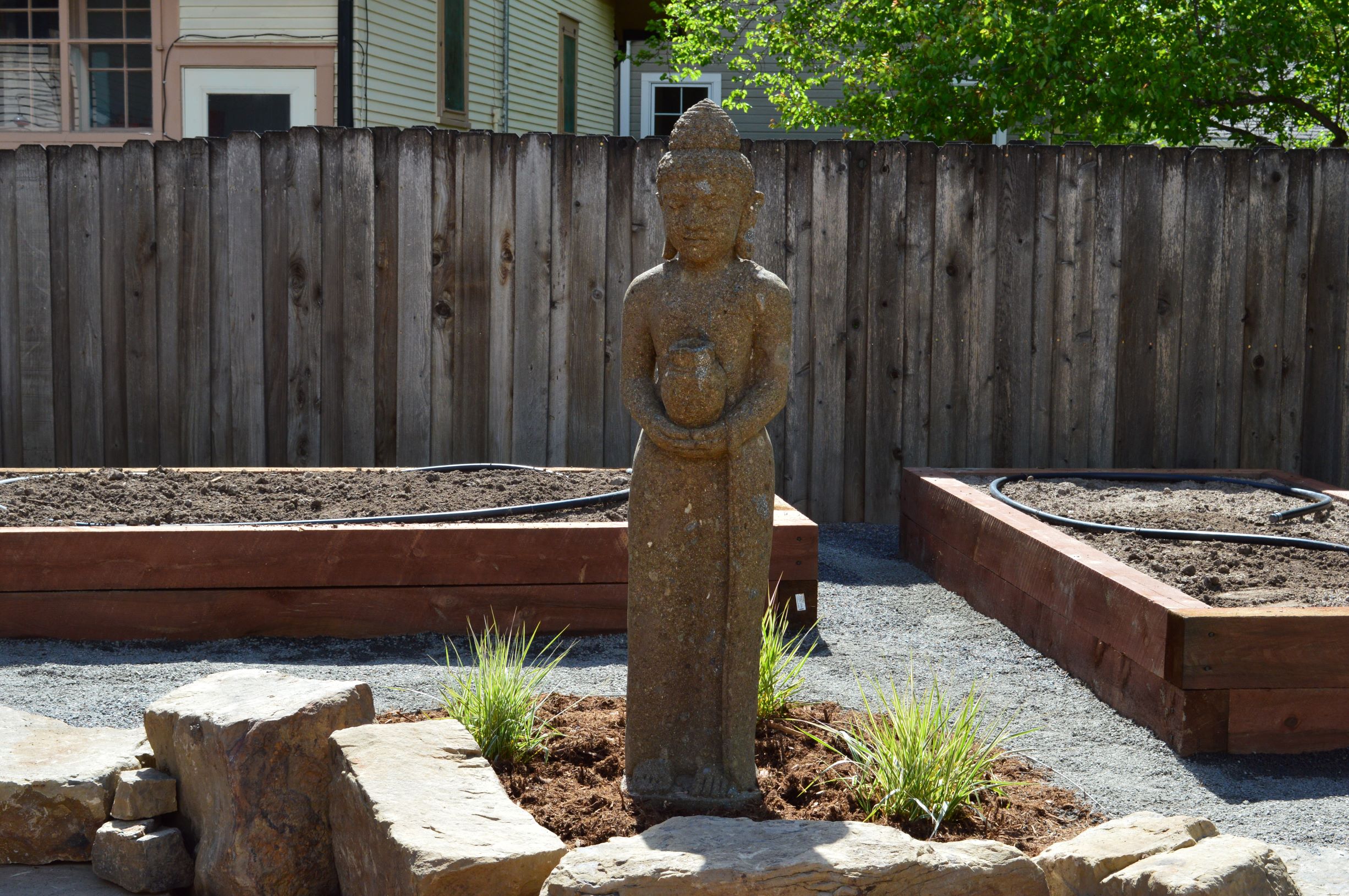 Statue placed in mulch surrounded by large decorative rock with flat stone steps and small gravel path.