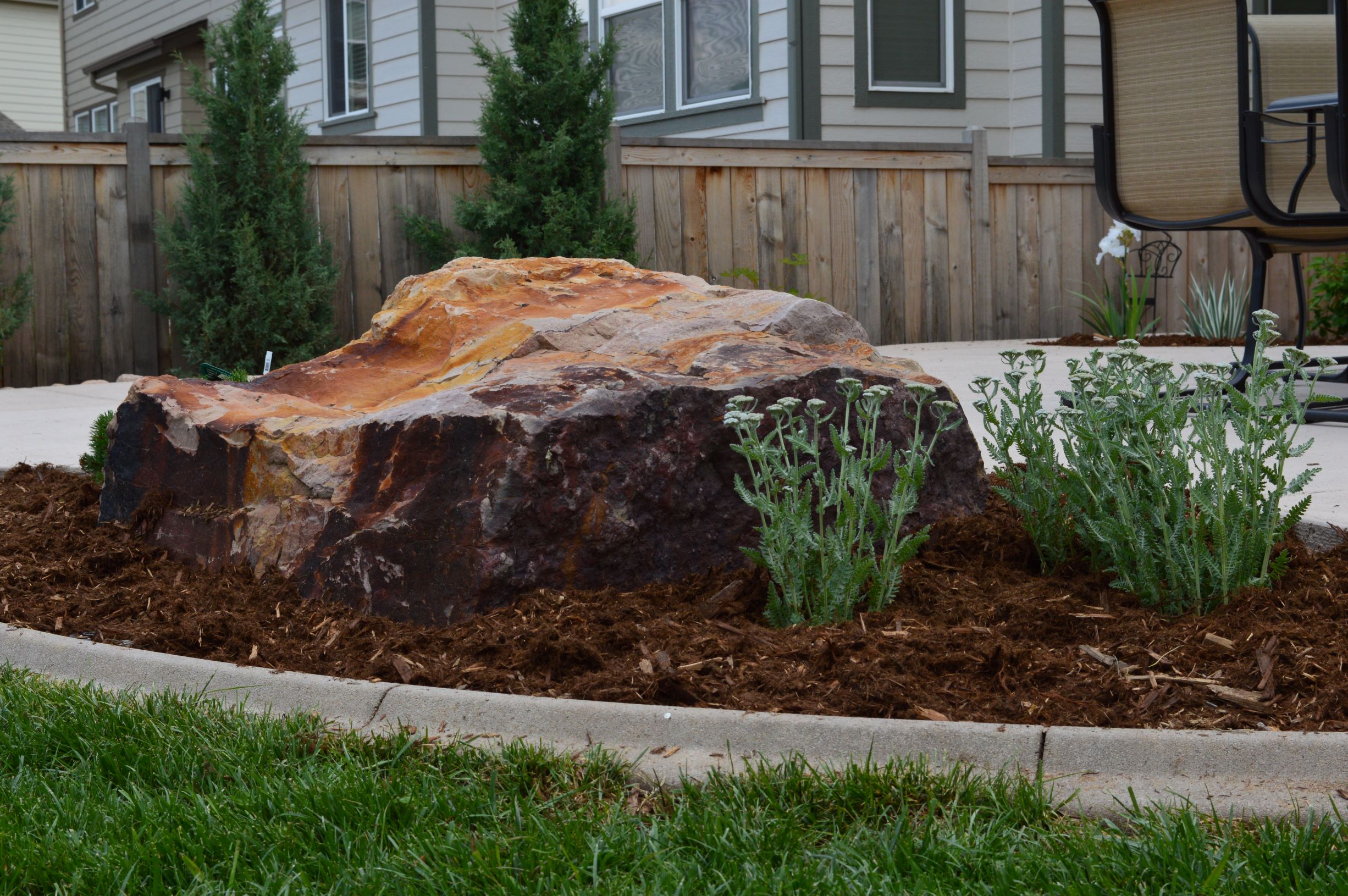 Large decorative rock with bushes and mulch around it.