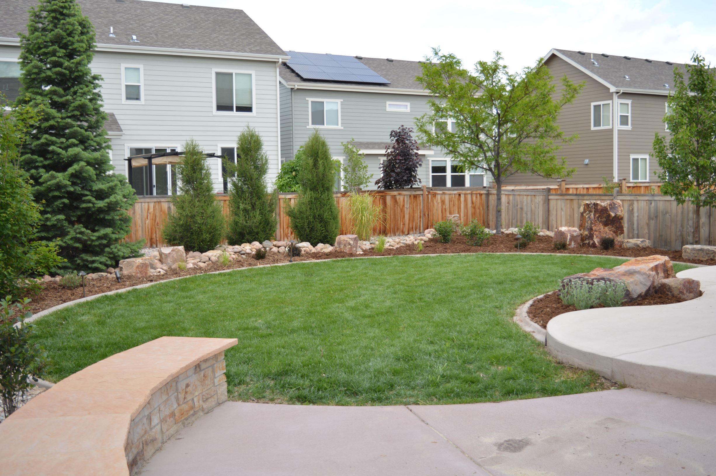 Concrete mow strip edged yard surrounded by mulch and large decorative rock.