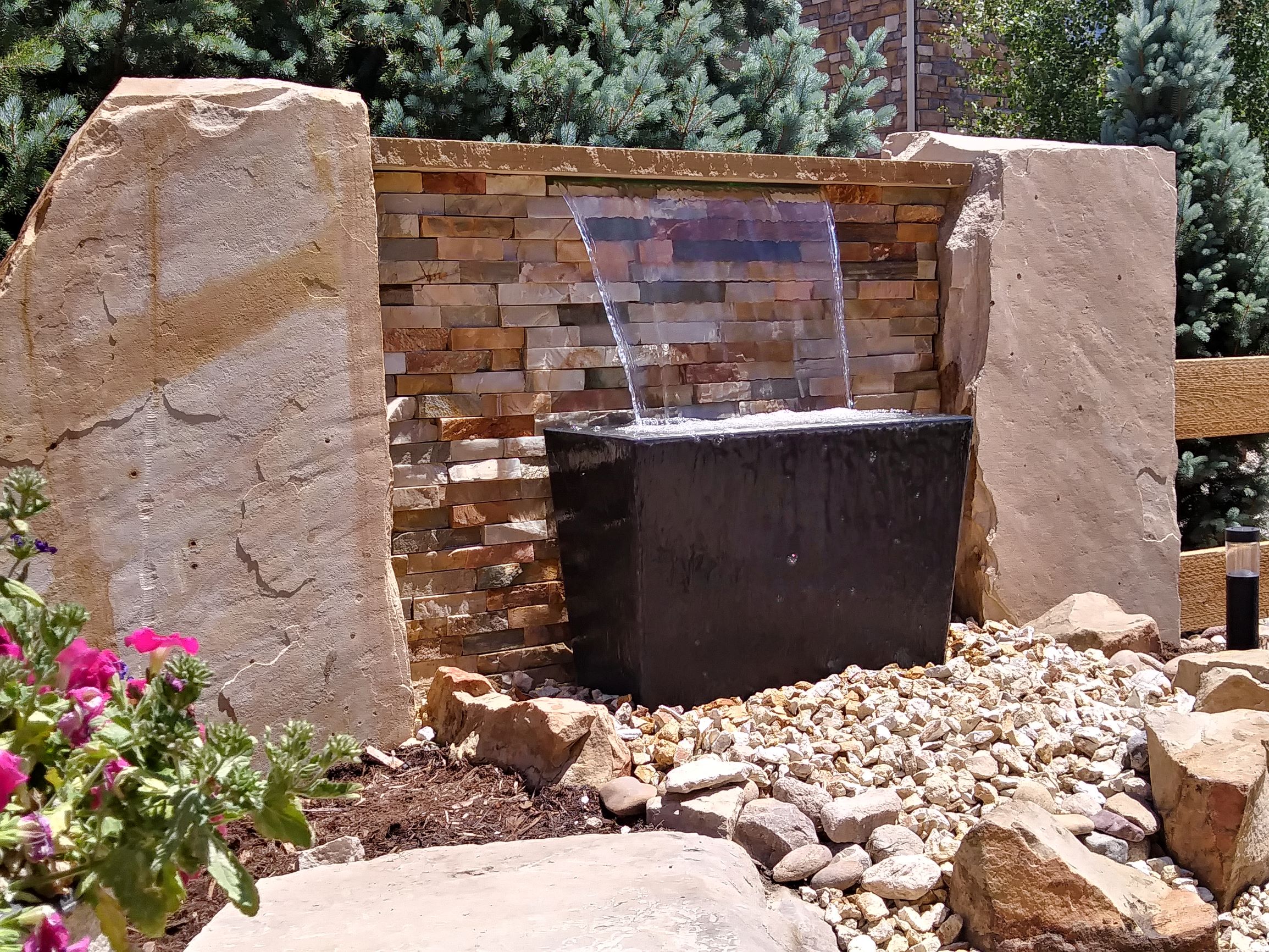 small water feature surrounded by stone, mulch, and decorative rock.