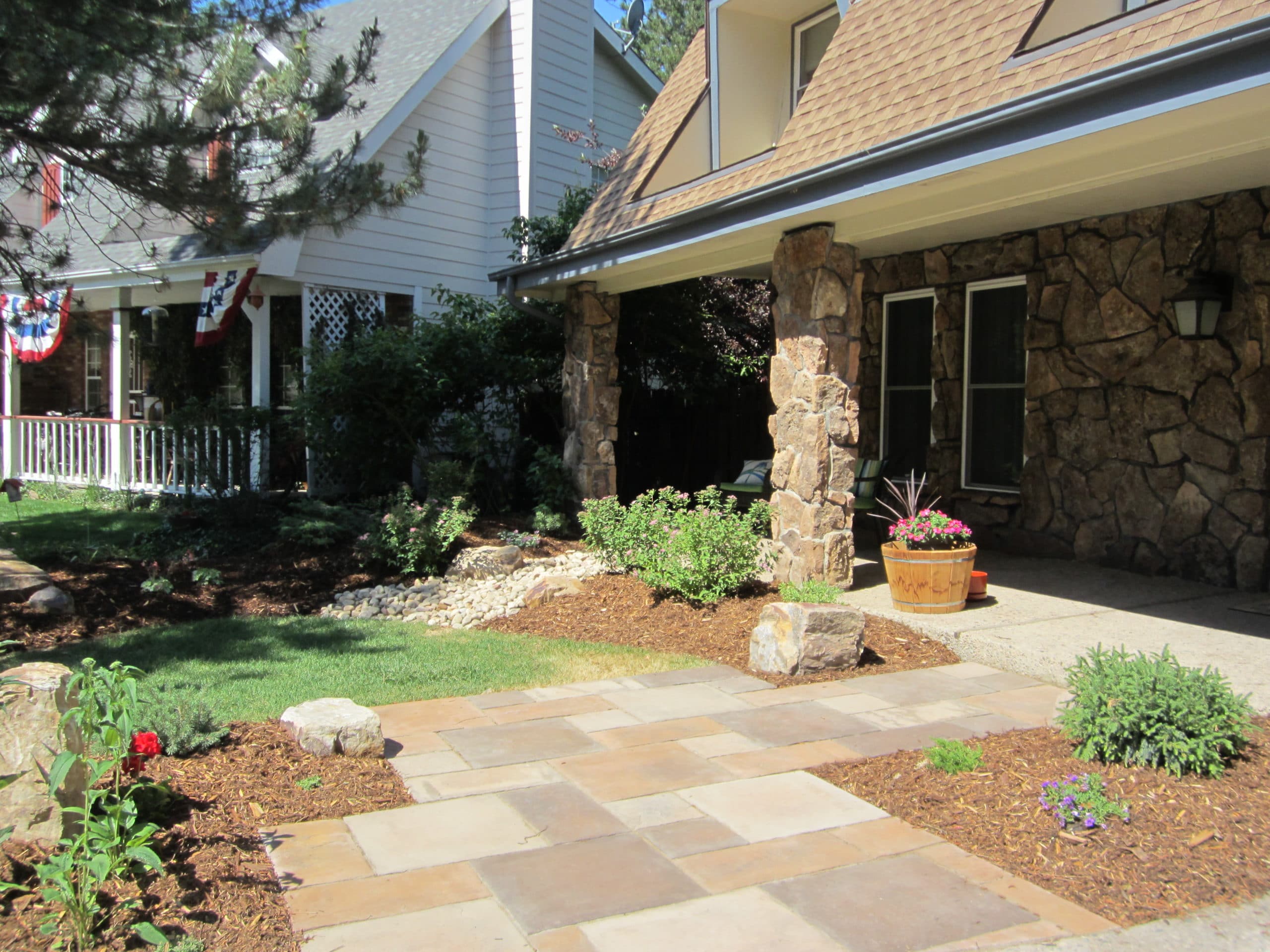 Brick laid path to front porch edged by grass and mulch with plants and bushes.