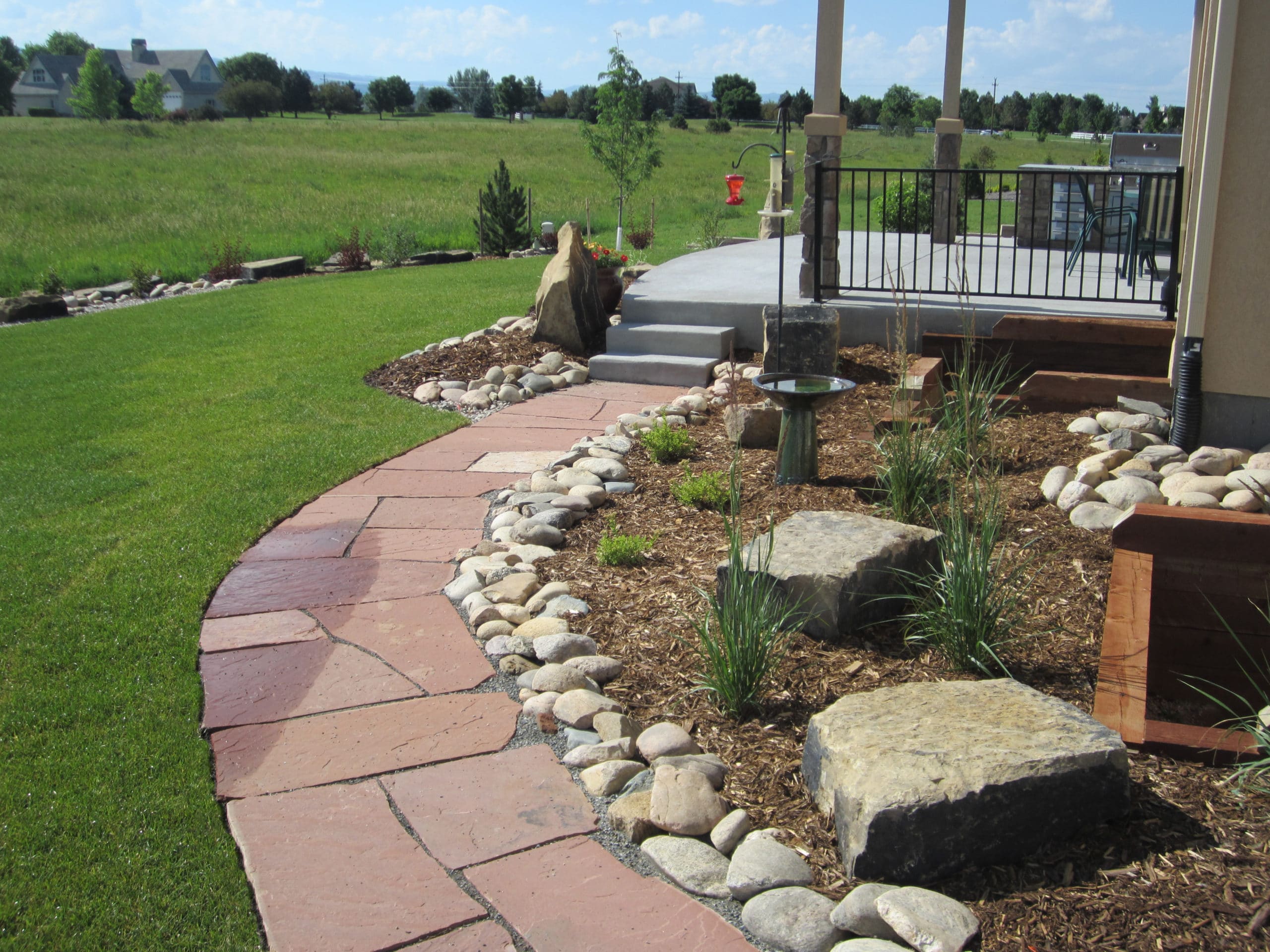 Flat stone path surrounded by green grass leading to a concrete patio.