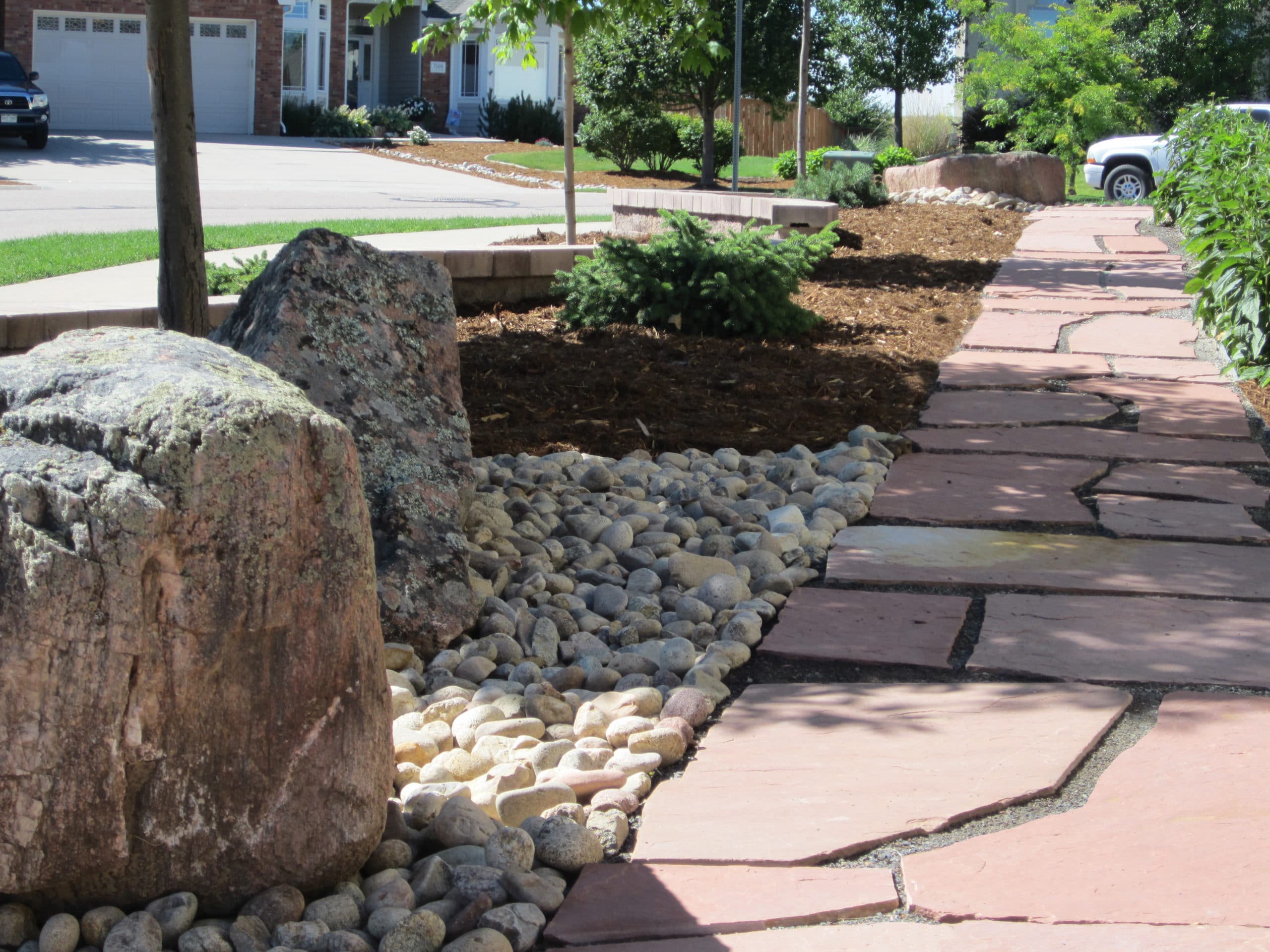Flat stone path in front of house with rock and mulch landscaping.