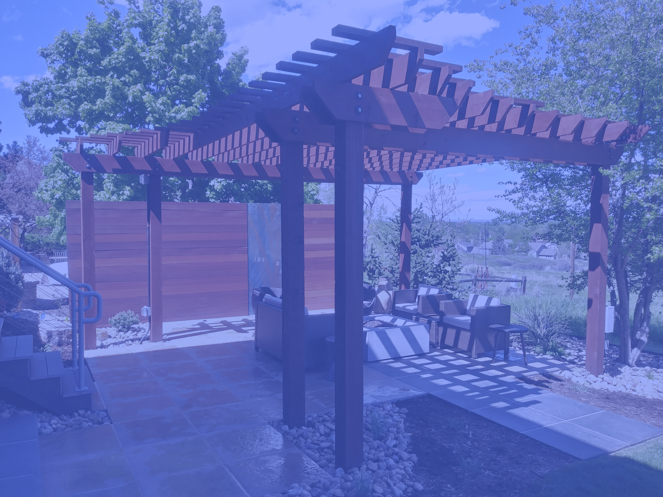 Pergola with flat tile patio and seating area blocked by wind/privacy wall.
